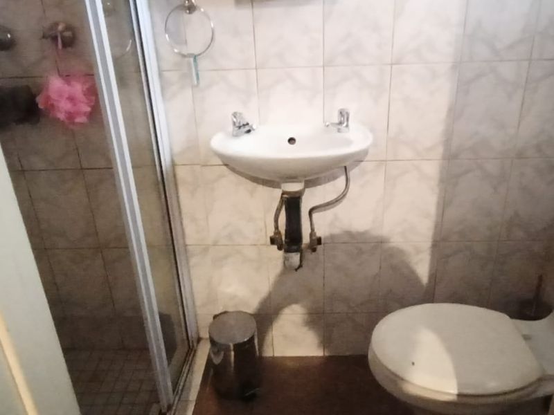 Compact bathroom featuring a shower enclosure, pedestal basin, and toilet with tiled wall finishes.