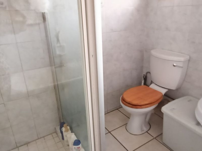 A functional bathroom featuring a shower enclosure, toilet, and washbasin with tiled walls and flooring throughout.