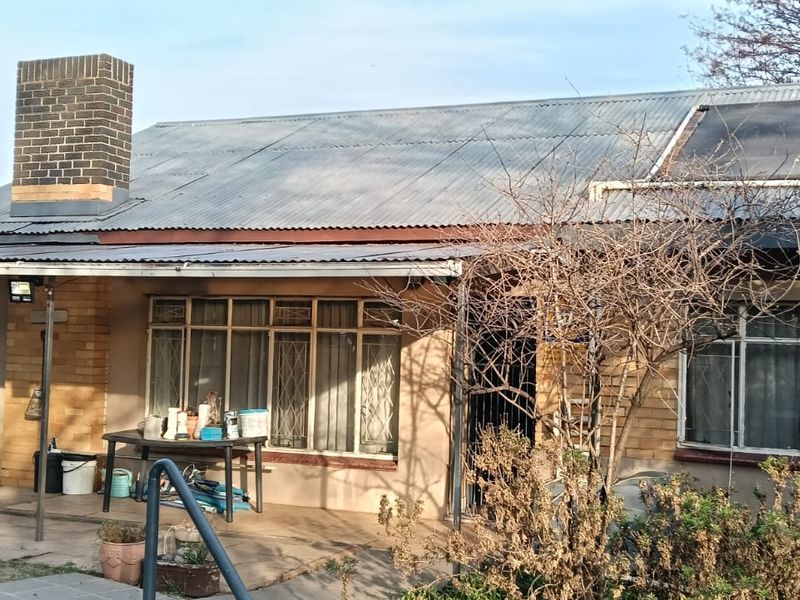Rear view of a single-story house featuring a corrugated iron roof, brick chimney, solar water heating panels, and a covered patio area.