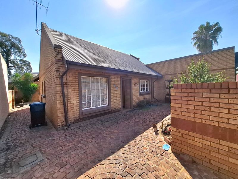 Front exterior view of a face brick house featuring a corrugated metal roof and a paved driveway area.