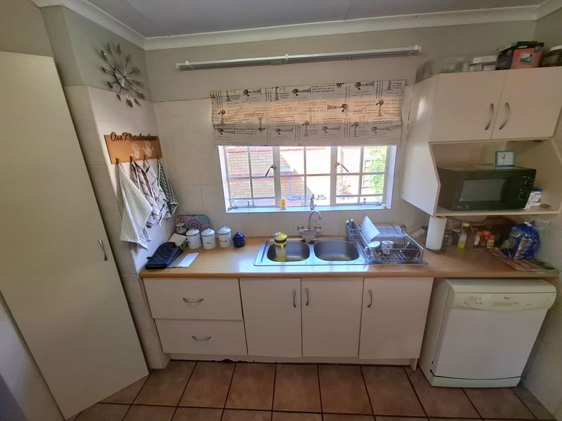 A functional kitchen area featuring a double bowl sink, laminate countertops, and built-in cabinetry with tiled flooring and splashbacks.