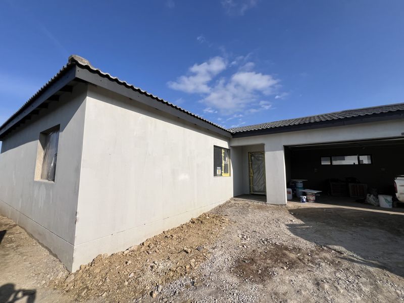 Exterior view of a house under construction featuring plastered walls, a tiled roof, and an integrated garage with unfinished surrounding grounds.