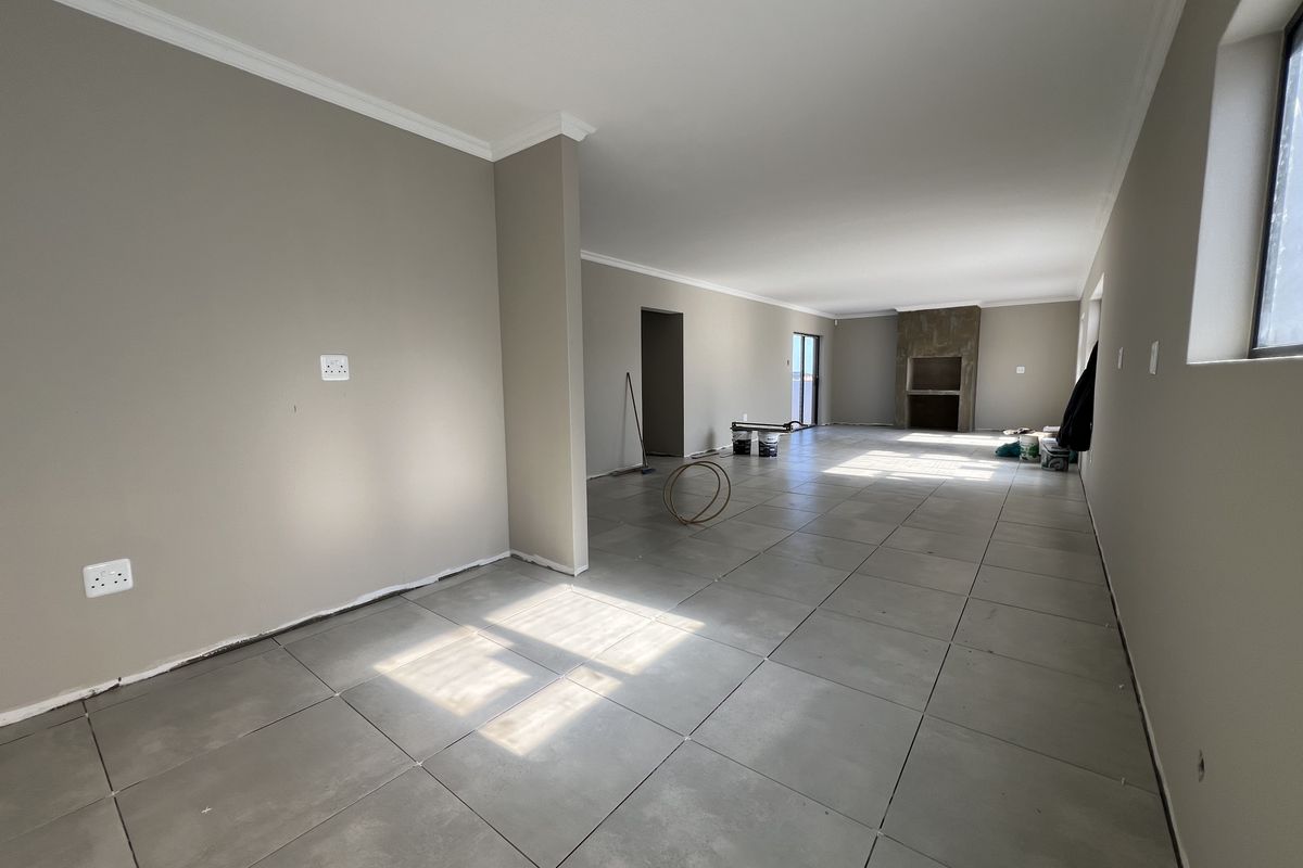 Spacious open-plan living area featuring large format floor tiles, neutral wall tones, and a prominent built-in fireplace.