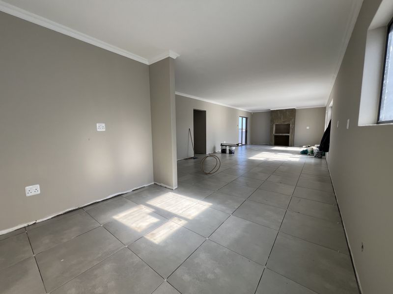 Spacious open-plan living area featuring large format floor tiles, neutral wall tones, and a prominent built-in fireplace.