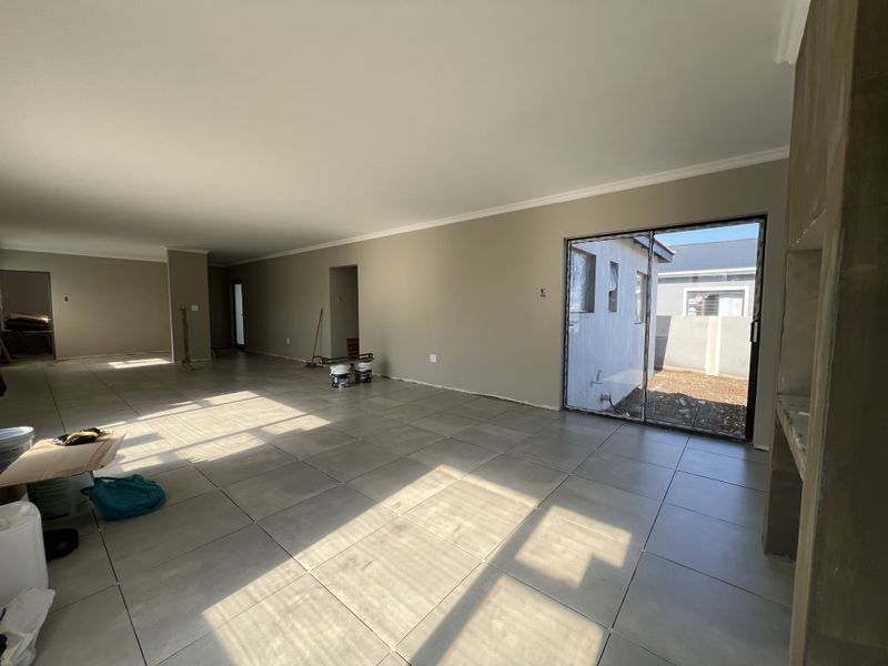 Spacious open-plan living area featuring large format floor tiles, a built-in fireplace, and sliding glass doors leading to the rear exterior.