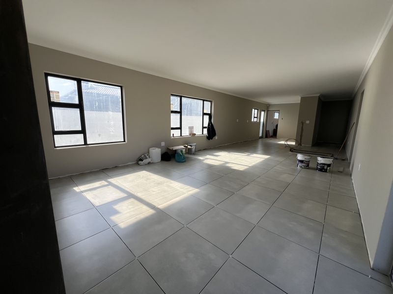 Spacious open-plan living area featuring large format floor tiles, neutral wall tones, and modern aluminium window frames, currently in a final stage of completion.