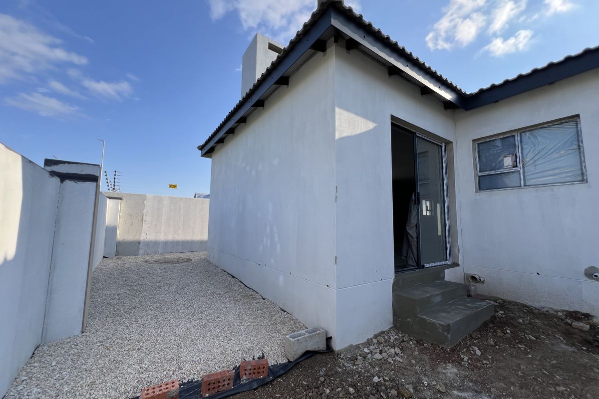 Rear exterior view of the property showing a sliding door entrance, concrete steps, and unfinished landscaping with gravel ground cover.