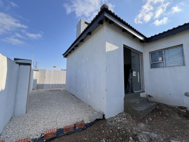 Rear exterior view of the property showing a sliding door entrance, concrete steps, and unfinished landscaping with gravel ground cover.