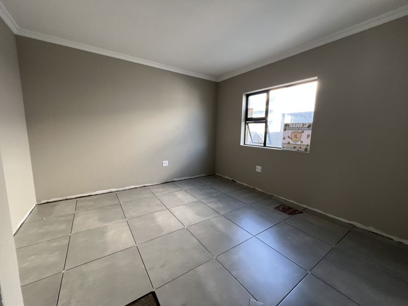 An empty bedroom featuring neutral wall paint, large format grey ceramic floor tiles, and an aluminium window frame. The room requires final finishing touches.