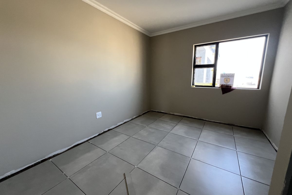 An empty bedroom featuring neutral painted walls, large format floor tiles, and an aluminium window frame, currently awaiting final finishing touches.