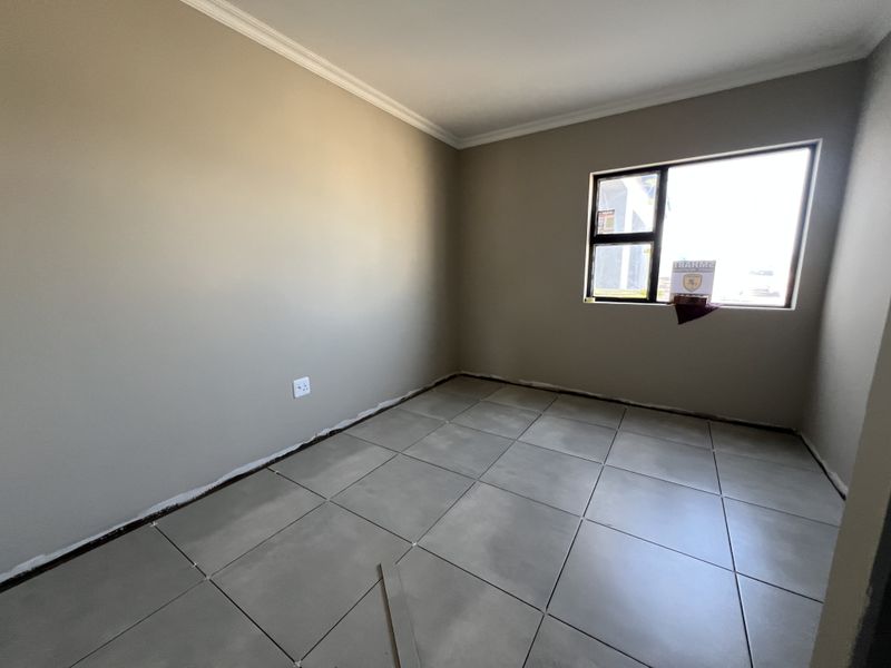 An empty bedroom featuring neutral painted walls, large format floor tiles, and an aluminium window frame, currently awaiting final finishing touches.