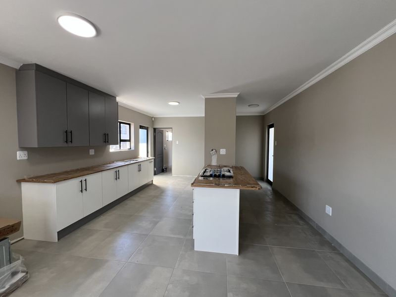Modern kitchen featuring two-tone cabinetry, wooden countertops, a central island with a hob, and neutral tiled flooring in an open-plan layout.