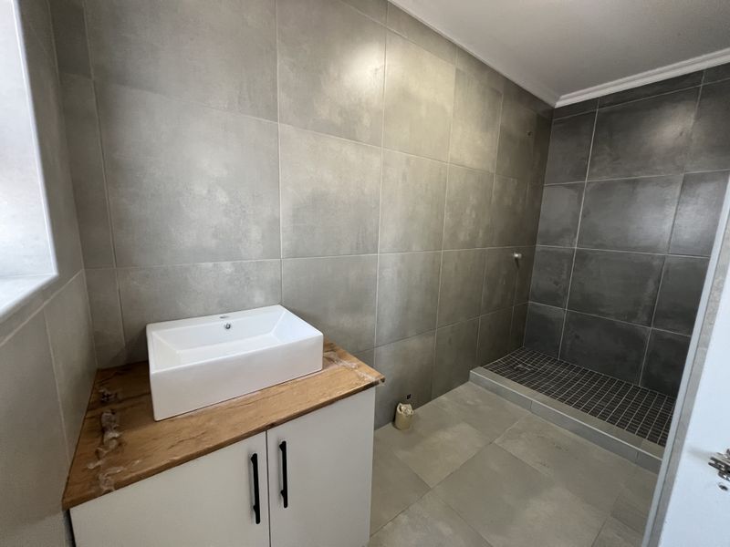 Modern bathroom featuring a vessel sink on a wooden vanity, large format grey wall tiles, and a walk-in shower with mosaic floor tiling.