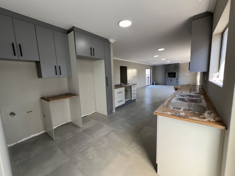 Spacious open-plan living and kitchen area featuring modern grey cabinetry, tiled flooring, and a built-in media unit, currently undergoing final finishing touches.