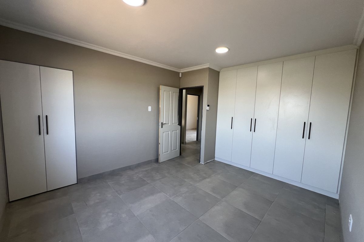 A spacious, empty bedroom featuring neutral tiled flooring, ample built-in cupboard storage, and modern recessed ceiling lighting.