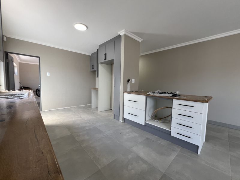 A modern, partially completed kitchen featuring grey and white cabinetry, a central island, and neutral tiled flooring, ready for final appliance installation.