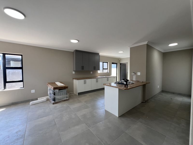 Modern open-plan kitchen featuring two-tone cabinetry, a central island, and neutral tiled flooring in a newly finished space.