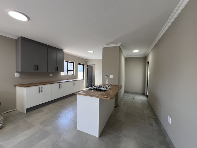 A modern, empty kitchen featuring two-tone cabinetry, wooden countertops, a central island, and neutral tiled flooring with recessed lighting.