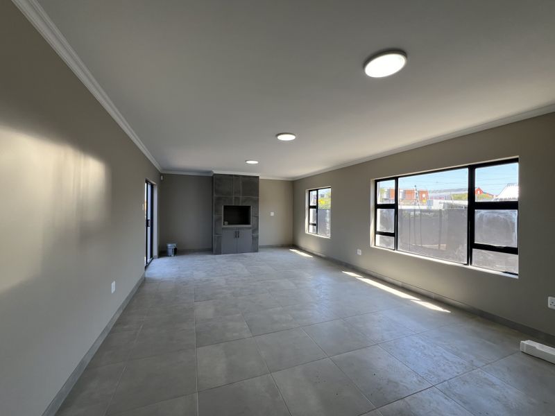 Spacious, modern living area featuring large format floor tiles, a built-in fireplace, and ample natural light through expansive aluminium-framed windows.