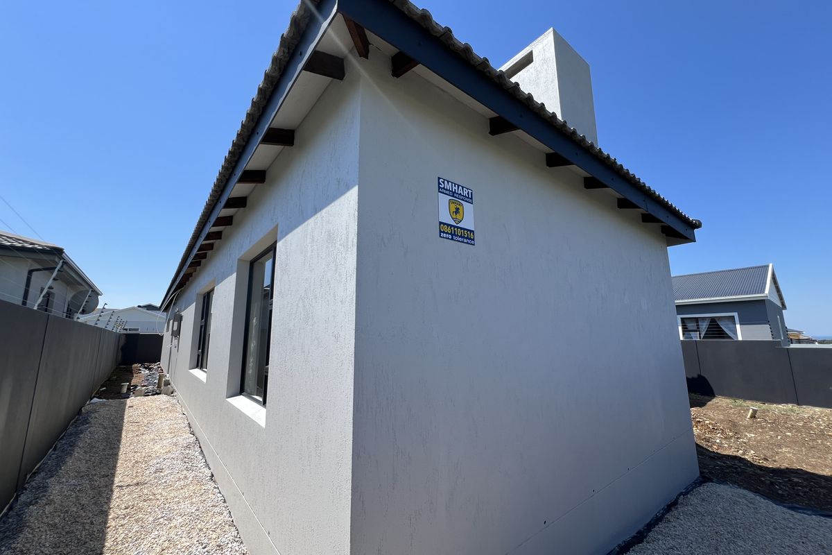 Rear exterior view of the property featuring a clean rendered facade, tiled roof with exposed rafters, a chimney, and a gravel side pathway.