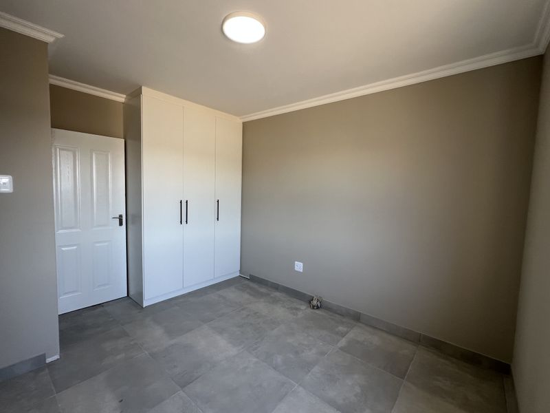 A clean, empty bedroom featuring neutral wall tones, modern grey floor tiles, and built-in white cupboards, offering a versatile space ready for personalization.