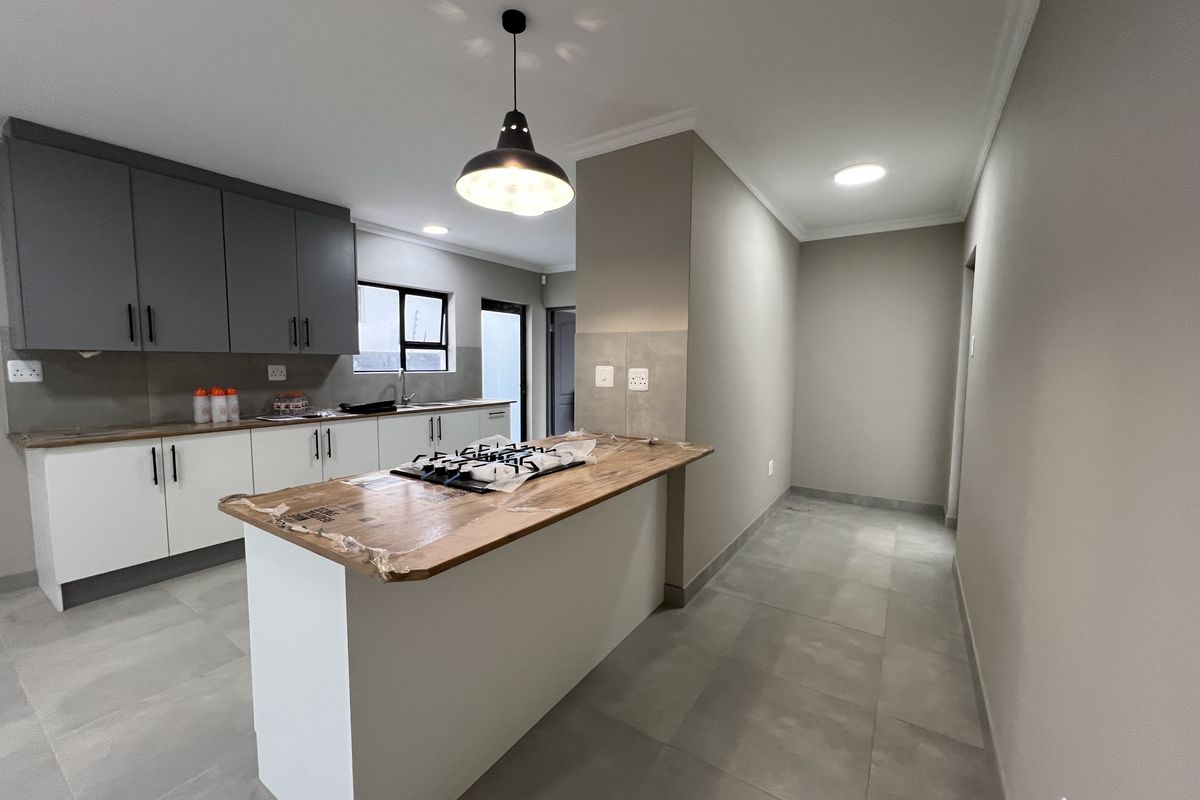 Modern kitchen featuring two-tone cabinetry, a central island with a gas hob, tiled flooring, and contemporary lighting fixtures in a clean, open space.