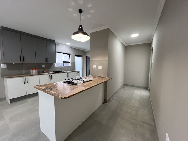 Modern kitchen featuring two-tone cabinetry, a central island with a gas hob, tiled flooring, and contemporary lighting fixtures in a clean, open space.