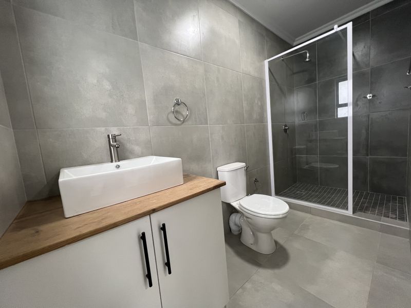 Modern bathroom featuring a walk-in shower with glass enclosure, a contemporary vanity with vessel sink, and neutral large-format wall and floor tiles.