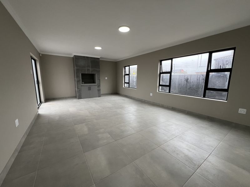 Spacious, modern living area featuring large tiled floors, a built-in fireplace, and ample natural light through contemporary aluminium-framed windows.