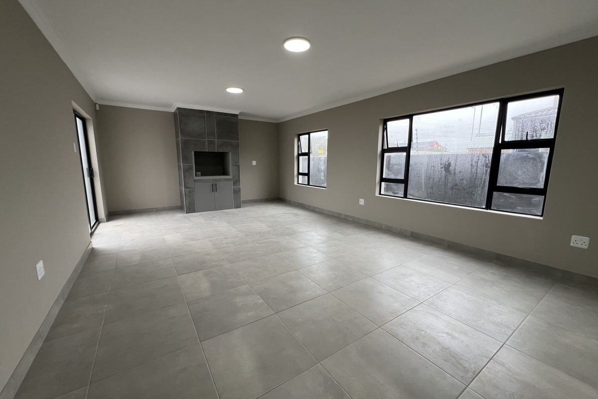 Spacious, modern living area featuring large tiled floors, a built-in fireplace, and ample natural light through contemporary aluminium-framed windows.