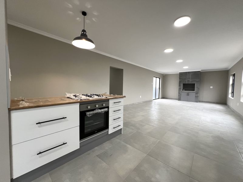 Spacious open-plan living area featuring a modern kitchen with built-in oven and hob, tiled floors, and a feature fireplace in the lounge area.