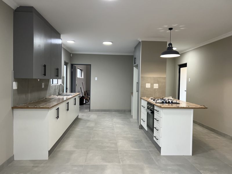 Modern kitchen featuring a central island with gas hob, built-in oven, ample cabinetry, and neutral tiled flooring in a clean, contemporary layout.