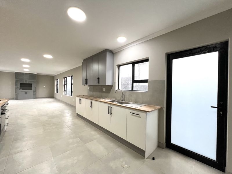 Spacious open-plan living area featuring a modern kitchen with built-in cabinetry, double sink, and a built-in fireplace, finished with neutral tiled flooring.