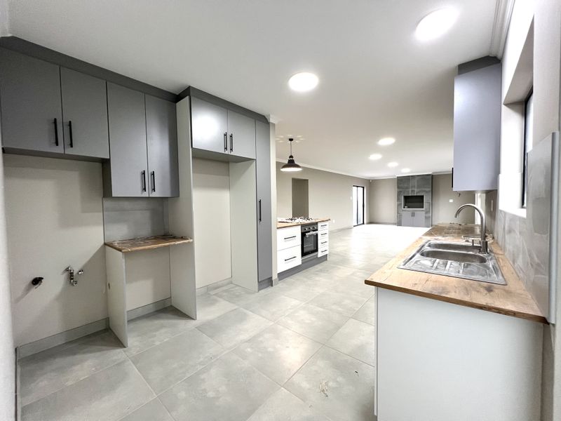 Modern open-plan kitchen and living area featuring sleek cabinetry, wood-look countertops, built-in appliances, and large format floor tiles in a bright, neutral space.