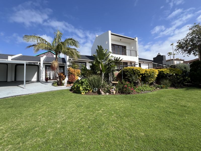 A well-maintained residential property featuring a landscaped front garden, paved driveway, double garage, and an upper-level balcony.