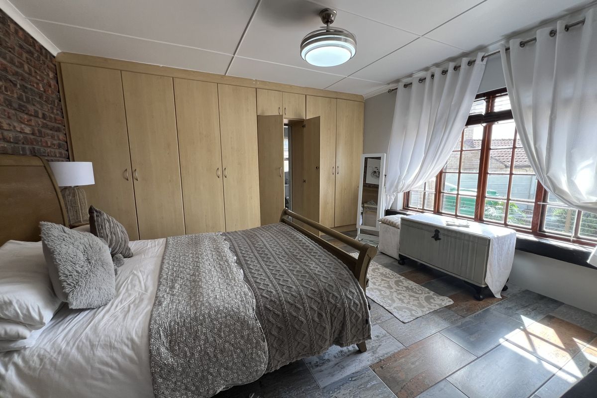 Spacious bedroom featuring extensive built-in cupboards, an exposed brick feature wall, and durable tiled flooring with natural light from the window.