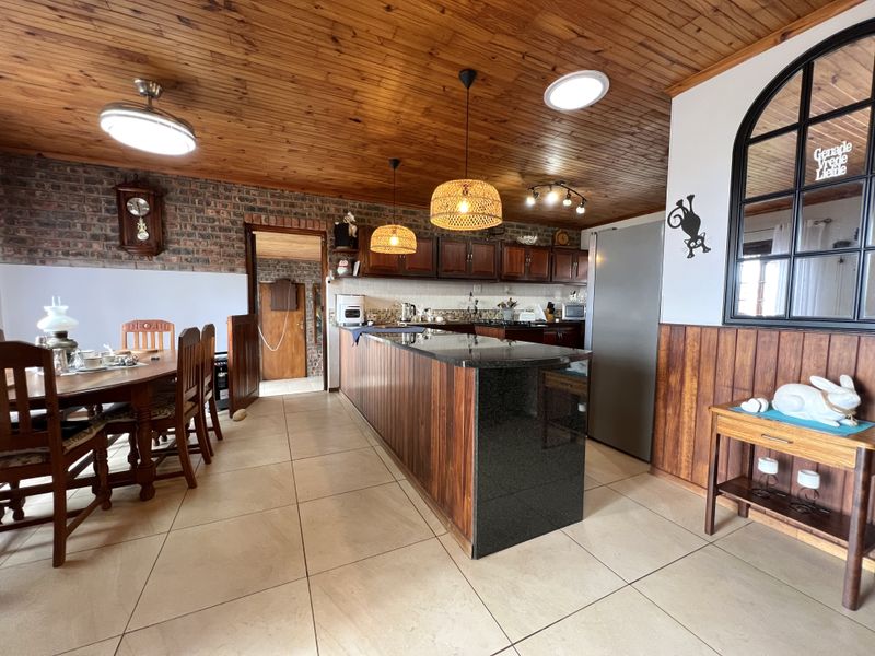 Open-plan kitchen and dining area featuring a granite island, timber cabinetry, exposed brick wall, and warm timber ceiling finishes.