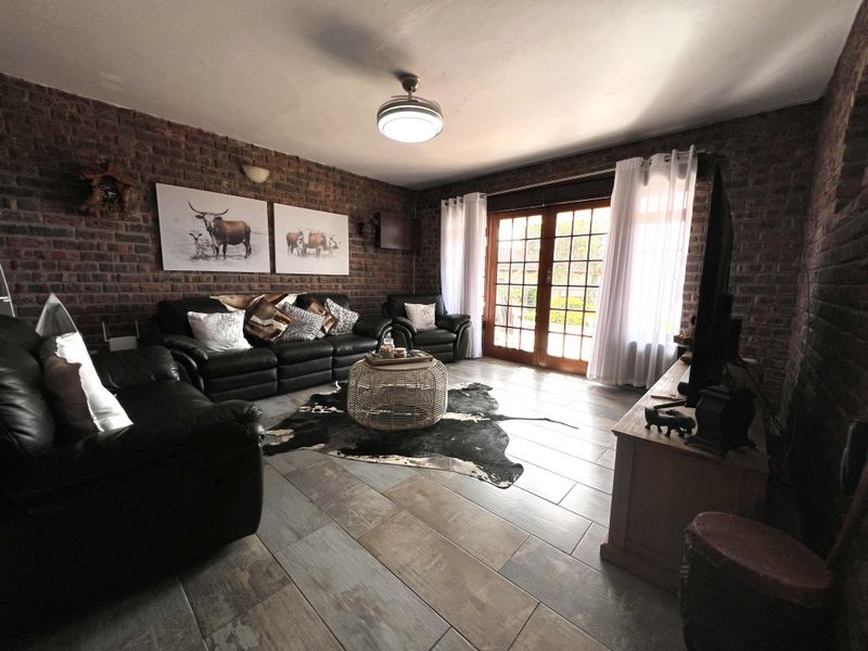 A cozy living room featuring rustic exposed brick walls, modern tiled flooring, and double french doors providing natural light and access to the outdoors.