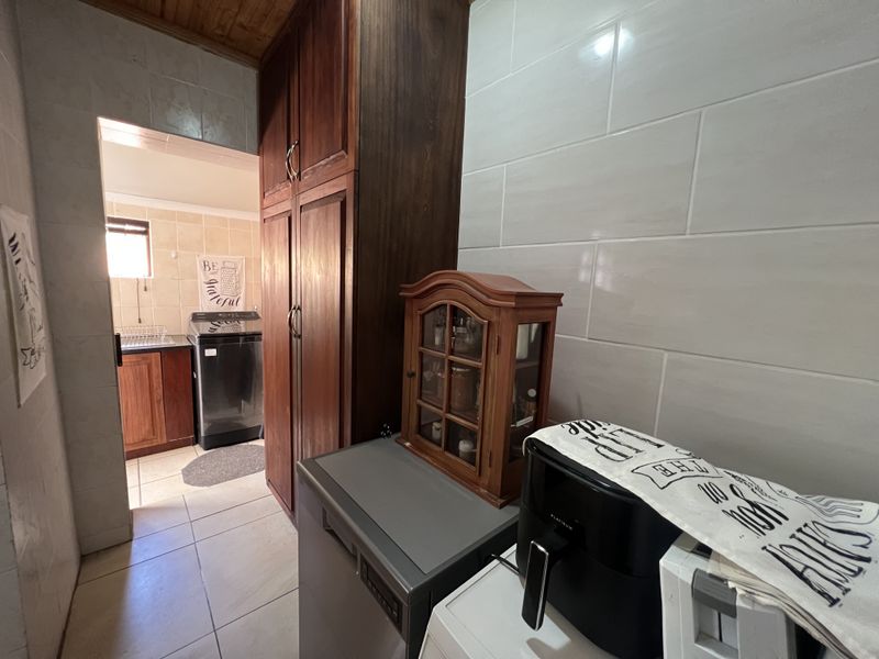 A functional scullery area featuring built-in wooden cabinetry, tiled walls, and timber ceiling, providing additional storage and utility space adjacent to the kitchen.