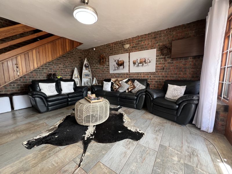 Spacious living room featuring a rustic exposed brick wall, tiled flooring, and a wooden staircase leading to the upper level.