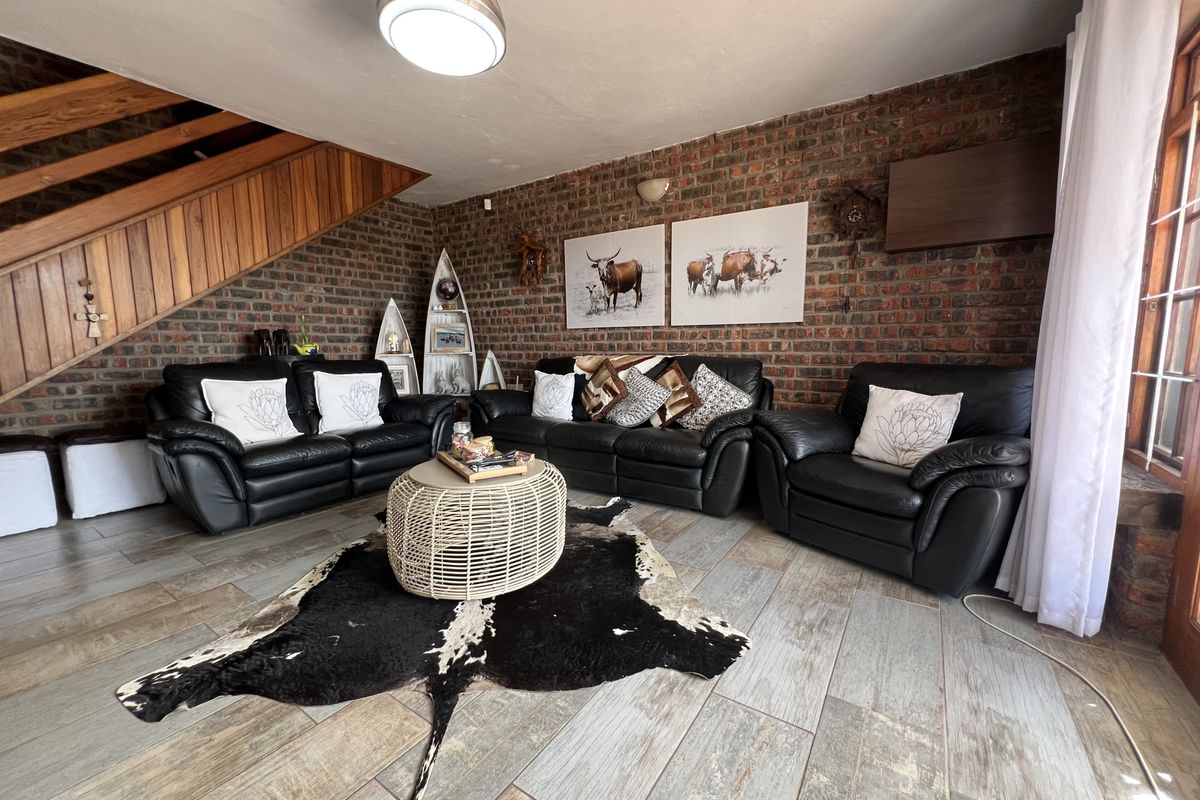 Spacious living room featuring a rustic exposed brick wall, tiled flooring, and a wooden staircase leading to the upper level.