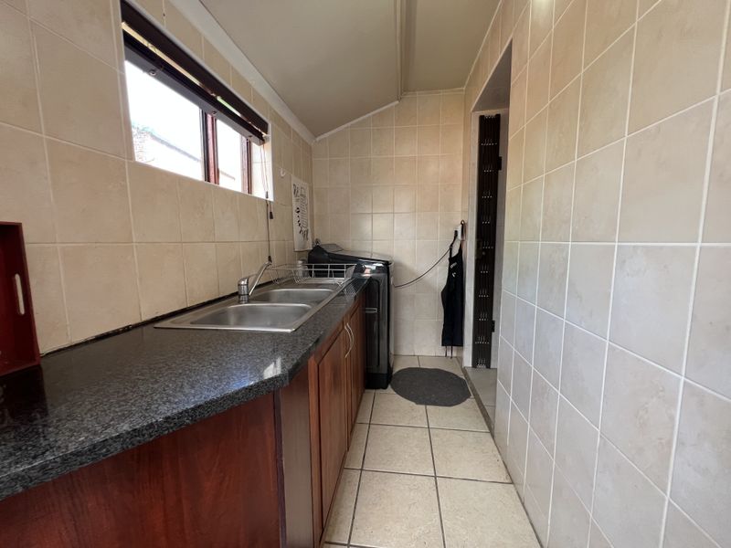 A functional laundry room featuring a double basin sink, granite countertops, built-in wooden cabinetry, and full-height ceramic wall tiling.