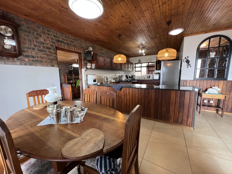 Open plan kitchen and dining area featuring timber ceilings, exposed brickwork, granite countertops, and warm wood cabinetry with tiled flooring throughout.