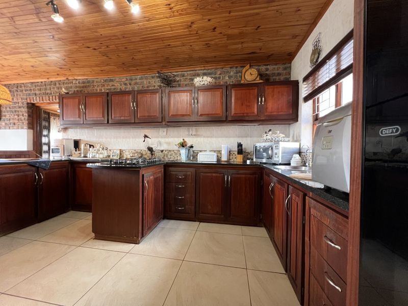 A spacious kitchen featuring warm timber cabinetry, granite countertops, a gas hob, and a distinctive timber-clad ceiling with exposed brick accents.