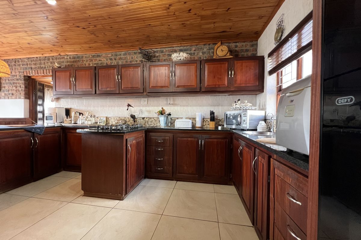 A spacious kitchen featuring warm timber cabinetry, granite countertops, a gas hob, and a distinctive timber-clad ceiling with exposed brick accents.