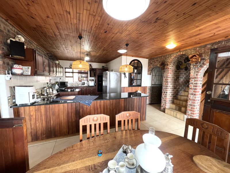 Open-plan kitchen and dining area featuring rustic exposed brick walls, wooden cabinetry, granite countertops, and a distinctive wooden tongue and groove ceiling.