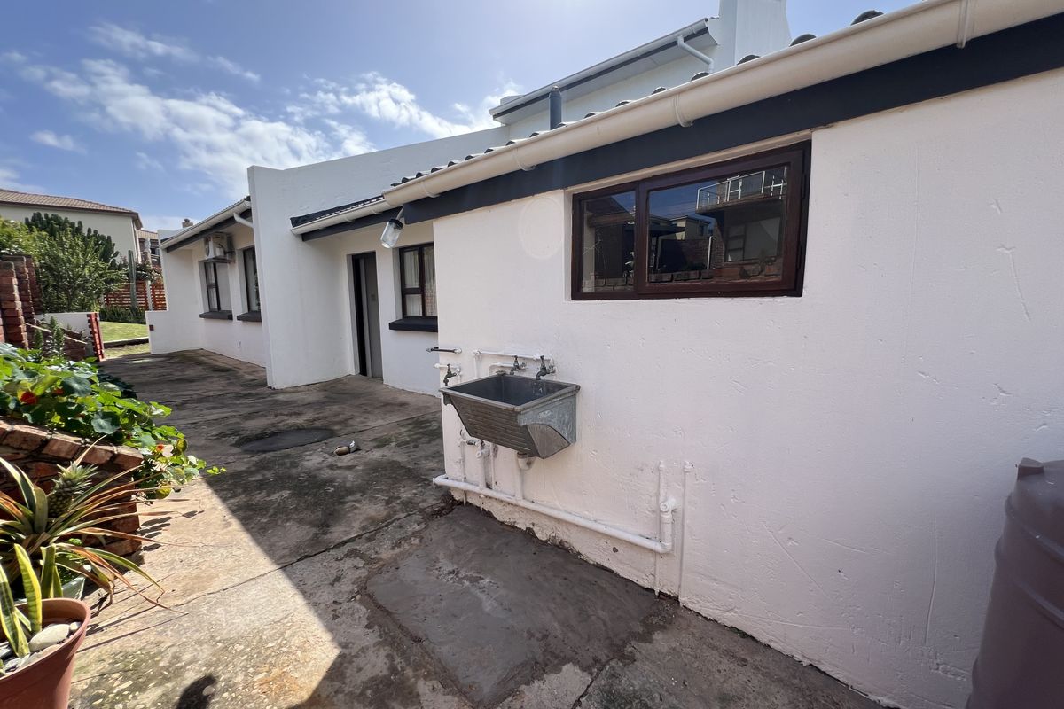 Rear exterior view of the property featuring a utility sink, concrete paving, and white rendered walls with dark window frames.