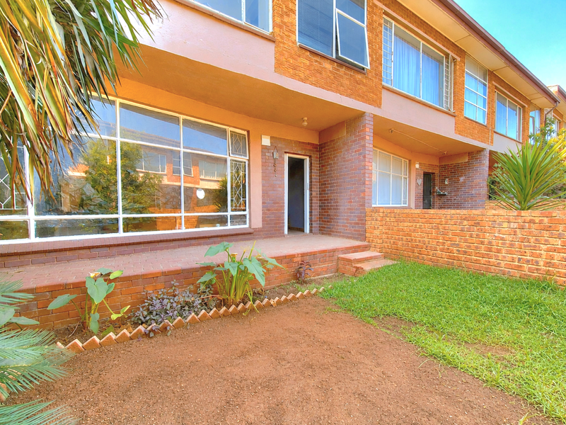 Front exterior view of an apartment unit featuring a brick facade, large steel-framed windows, a private patio area, and a small garden space.