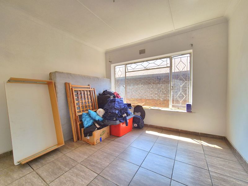 A bedroom featuring tiled flooring and a window with security bars, currently used for storage.
