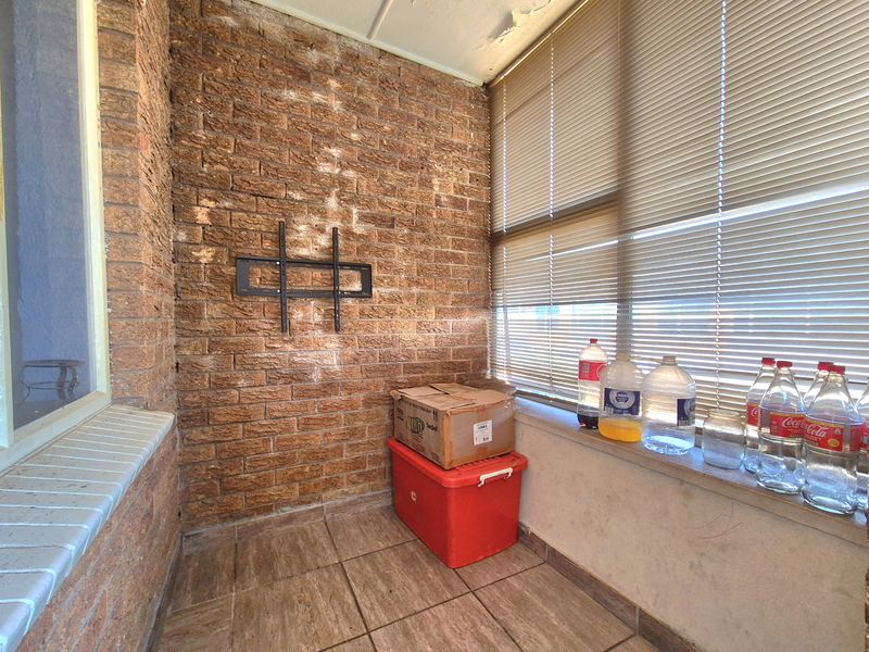 Enclosed balcony area featuring exposed brick walls, tiled flooring, and venetian blinds, requiring maintenance to the ceiling and brickwork finishes.
